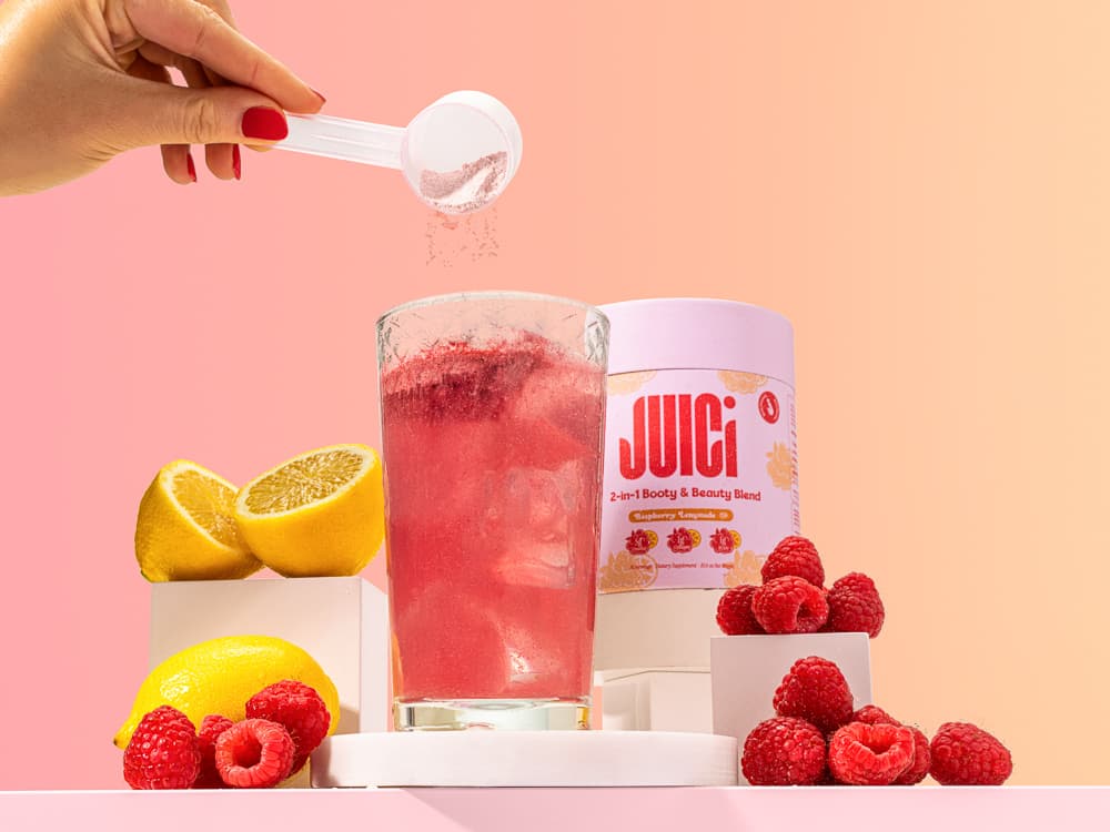 JUICI raspberry lemonade photographed with fruit, a glass and a pouring scoop against pink