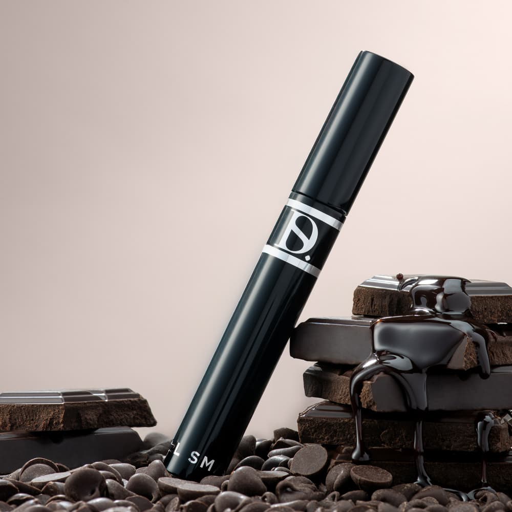 Black cosmetic product beside chocolate pieces